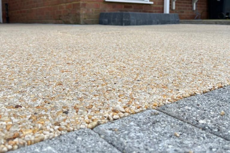 Resin overlay surface laid over an existing driveway beside grey block paving edging